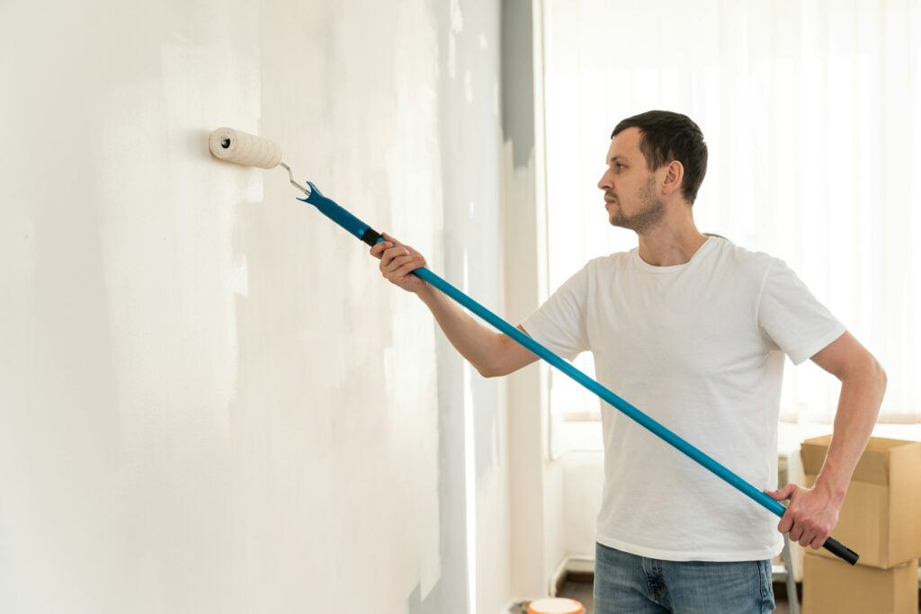 Male painter. Concentrated dark haired man holding dirty paint roller and preparing to repair walls