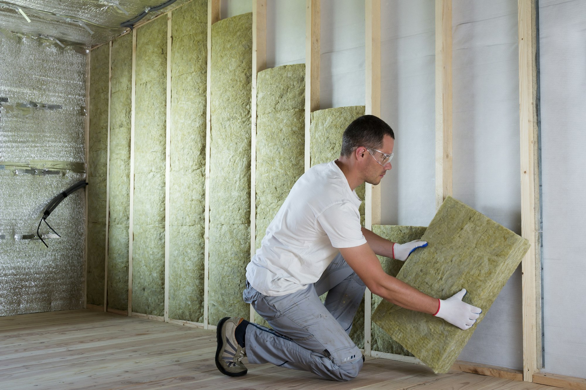 Worker in protective goggles and respirator insulating rock wool insulation